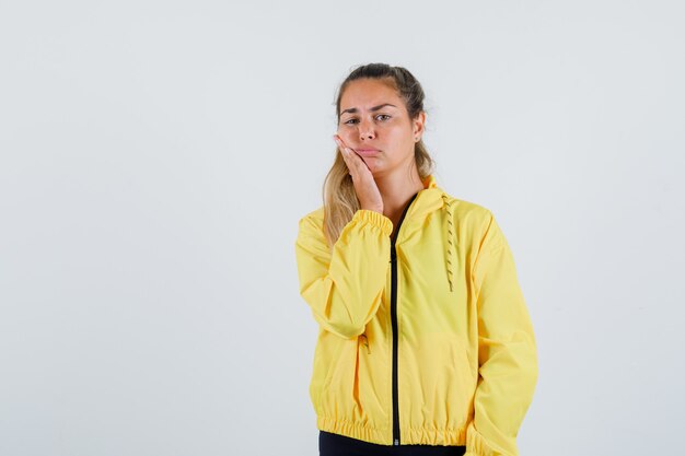 Mulher jovem tocando a bochecha com uma capa de chuva amarela e parecendo dolorida