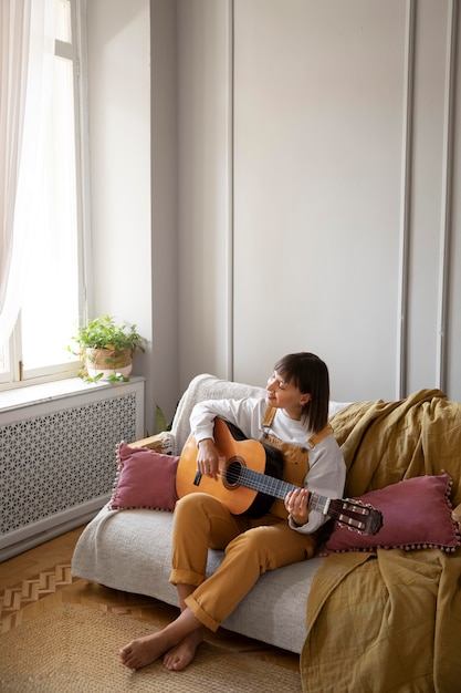 Mulher jovem tocando violão dentro de casa com espaço de cópia