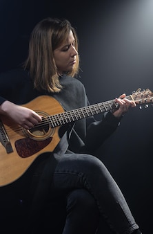 Mulher jovem tocando violão em um quarto escuro com neblina