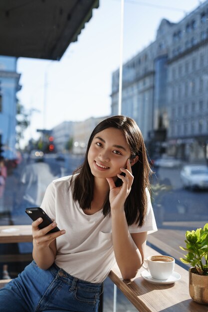 Mulher jovem tomando café em um restaurante num dia de verão, conversando no smartphone