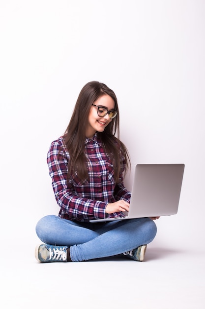 Mulher jovem trabalhando em um laptop no chão, sobre um fundo branco