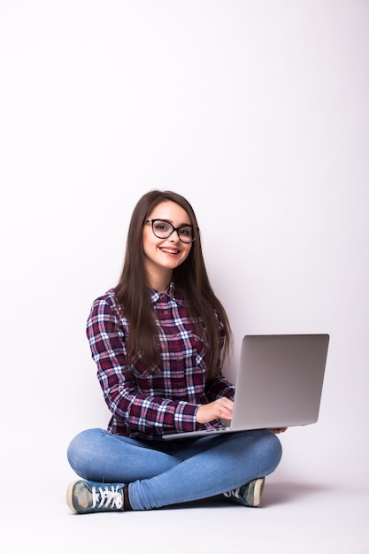 Mulher jovem trabalhando em um laptop no chão, sobre um fundo branco