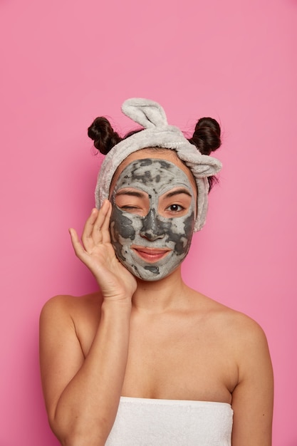 Mulher jovem usa máscara facial natural de argila para tratamentos de pele após o banho