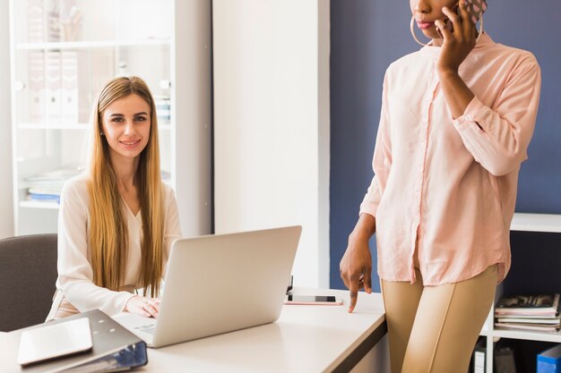 Mulher jovem, usando computador portátil, perto, colega colheita, com, smartphone