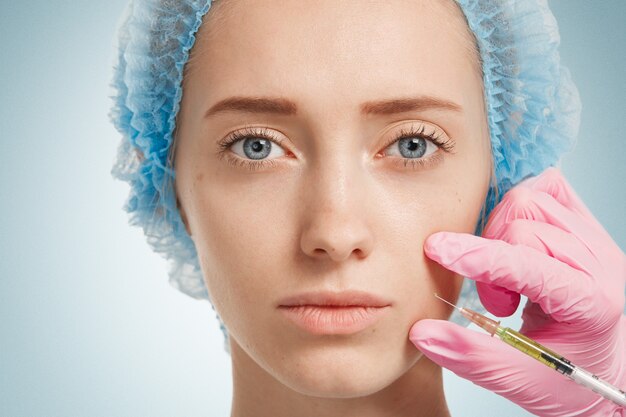 Mulher jovem usando touca médica enquanto o médico injeta no rosto