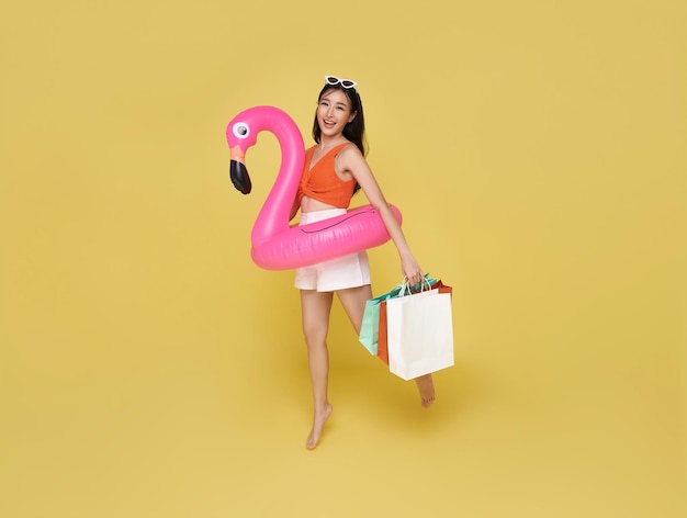 Foto grátis mulher jovem vestida com trajes de banho segurando saco de compras e anel de borracha de flamingo pulando para o verão