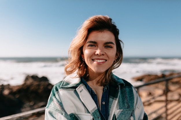 Mulher jovem vestindo camisa jeans e sorrindo posando na praia