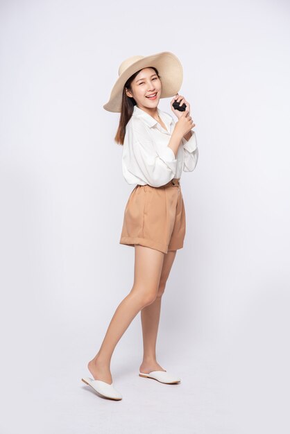 Mulher jovem vestindo uma camisa branca e shorts, usando um chapéu e alça no chapéu