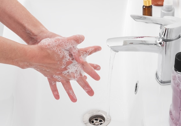 Mulher lava as mãos com sabonete embaixo da torneira do banheiro