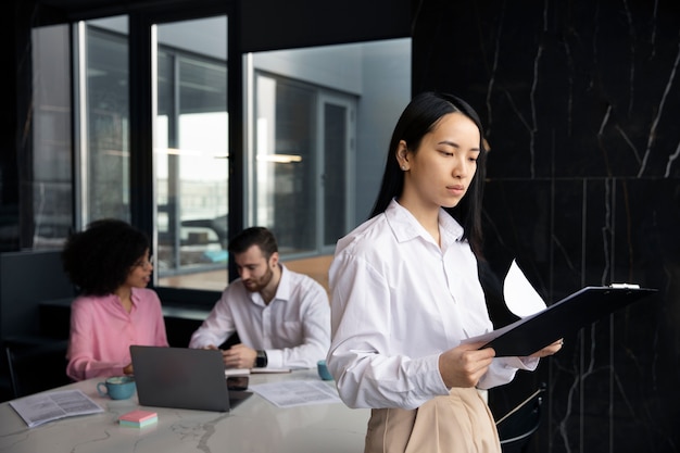 Mulher lendo documentos para o trabalho enquanto seus colegas estão usando um laptop