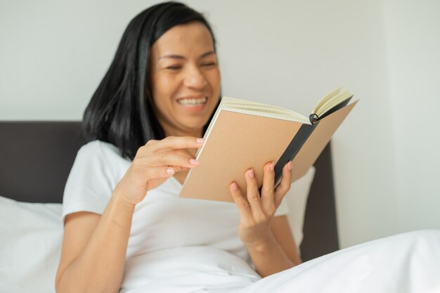 Mulher lendo livro em casa no quarto.