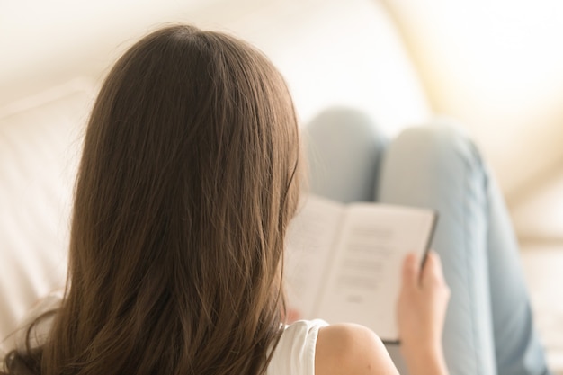 Mulher lendo livro interessante no sofá em casa