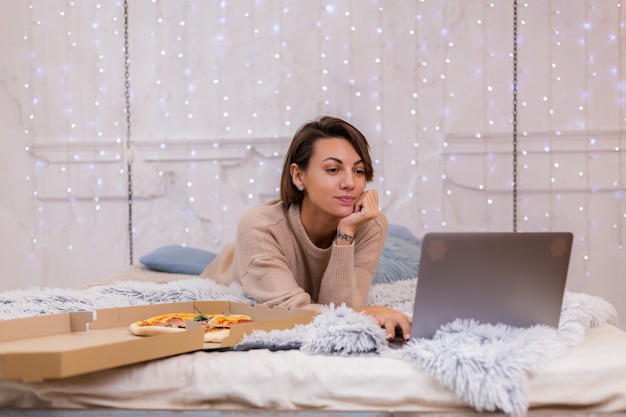 Mulher leste fast-food de entrega na cama no quarto em casa. mulher sozinha apreciando comida gordurosa, pizza