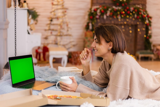 Mulher leste fast-food pizza de entrega na cama, no quarto em casa na época do ano novo de Natal.