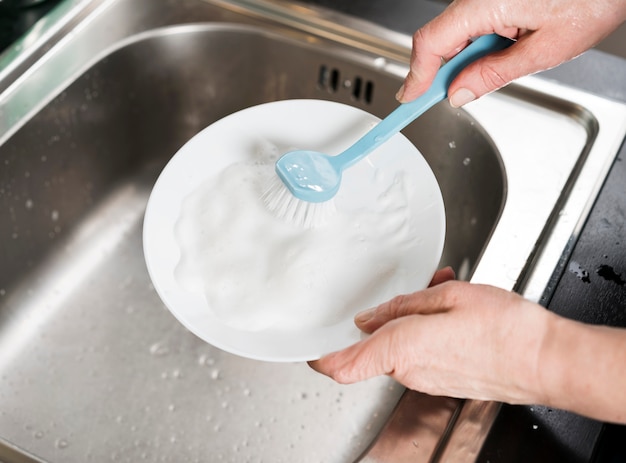 Mulher limpando o prato na pia com escova