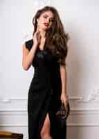 Foto grátis mulher linda e deslumbrante com lábios carnudos vermelhos, olhos esfumados e cabelos ondulados perfeitos em um elegante vestido preto casual posando