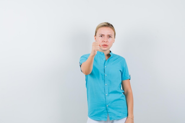 Mulher loira ameaçando com o punho na blusa azul e parecendo totalmente isolada