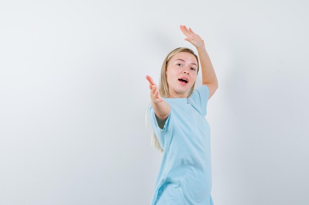 Mulher loira apontando com o dedo indicador em uma camiseta azul e parecendo feliz