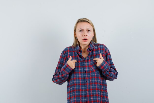 Mulher loira apontando para si mesma em uma camisa e parecendo surpresa. vista frontal.