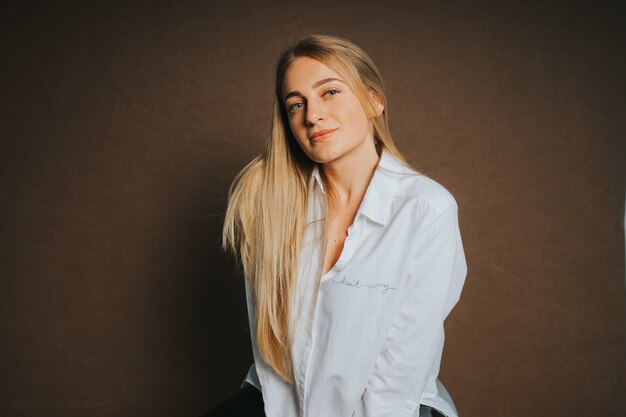 Mulher loira atraente, branca com uma camisa branca, posando em um marrom