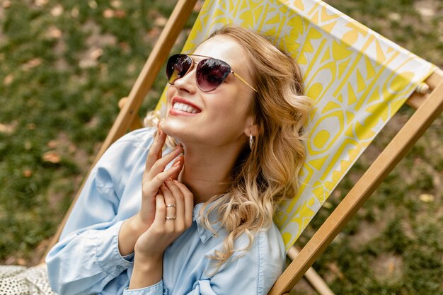 Mulher loira atraente e sorridente sentada em uma espreguiçadeira com roupa de verão
