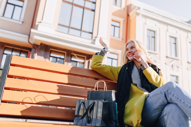Foto grátis mulher loira atraente feliz fofa com pacotes na rua em tempo ensolarado