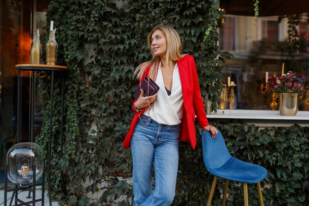 Mulher loira bonita e bonita com jaqueta vermelha posando em um café da cidade