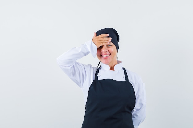 Mulher loira cobrindo a testa com a mão no uniforme preto de cozinheira e bonita