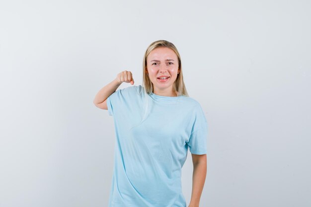 Mulher loira com camiseta azul cerrando os punhos e parecendo confiante