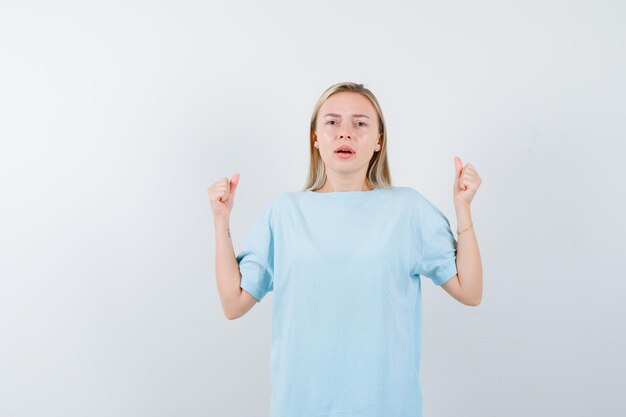 Mulher loira com camiseta azul mostrando gesto de vencedor e parecendo com sorte