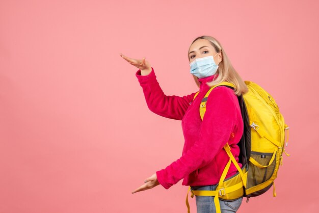 Mulher loira com mochila amarela e máscara mostrando o tamanho com as mãos