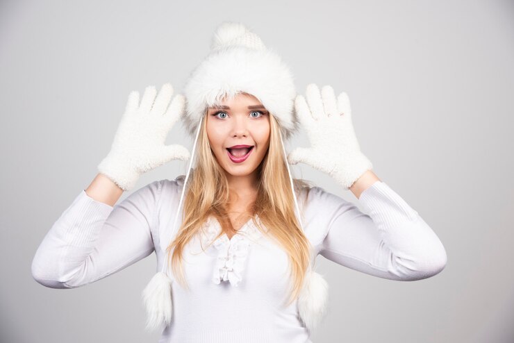 Foto grátis mulher loira com roupa de inverno, agindo de surpresa na parede cinza.
