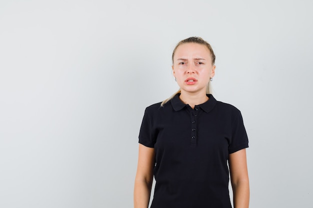 Mulher loira com uma camiseta preta tentando dizer algo e parecendo confusa