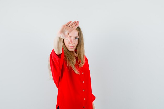 Mulher loira de camisa vermelha mostrando gesto de pare e parecendo decidida,