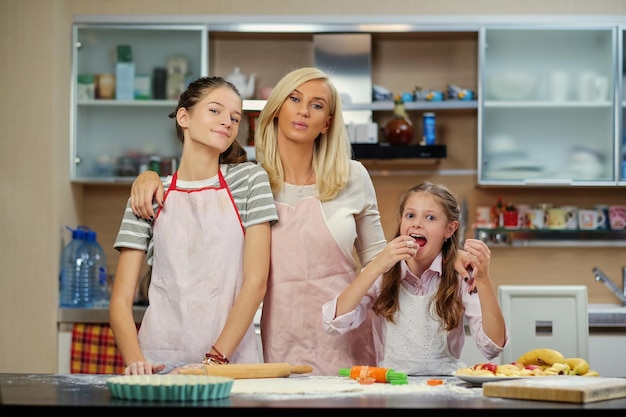 Mulher loira e duas adolescentes mostrando como massa na cozinha de casa.