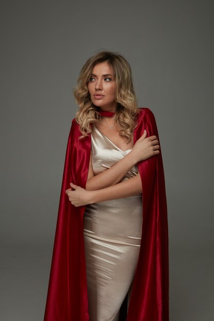 Mulher loira elegante com vestido longo brilhante e capa de seda vermelha