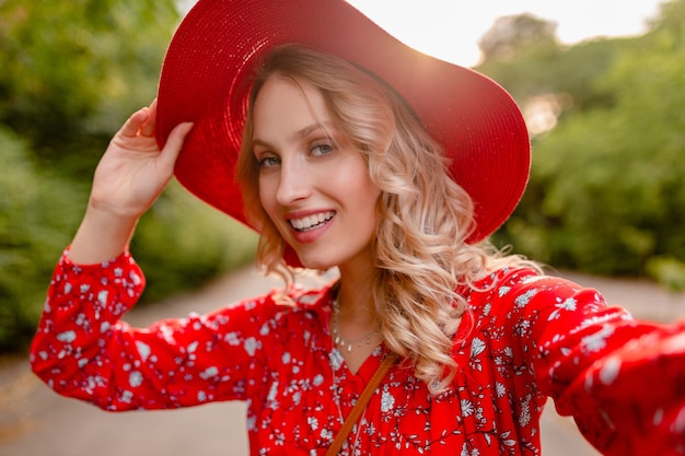 Mulher loira elegante e atraente e sorridente com chapéu vermelho palha e blusa, roupa da moda de verão, tirando foto de selfie