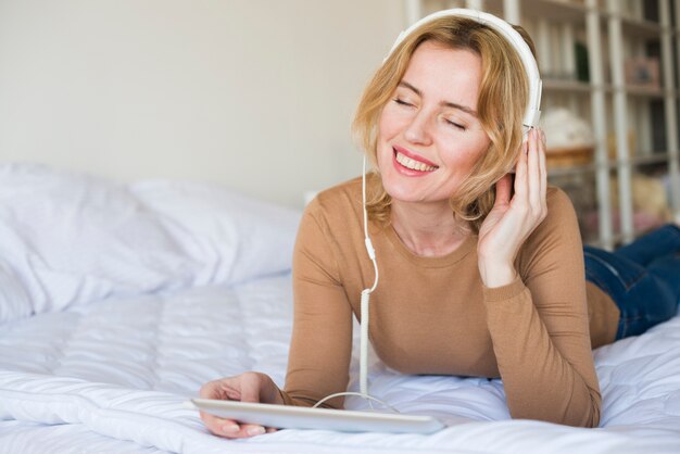 Mulher loira em fones de ouvido, ouvindo música na cama