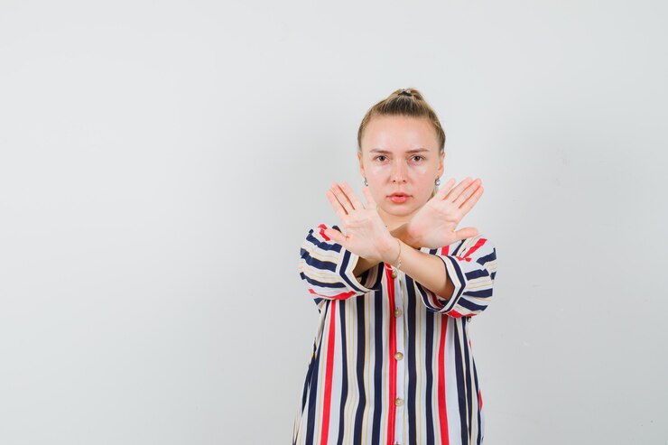 Foto grátis mulher loira em pé com as mãos cruzadas e mostrando um gesto de parada com uma blusa listrada e olhando séria