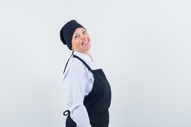 Mulher loira em pé em linha reta e posando na frente em uniforme de cozinheiro preto e está linda.
