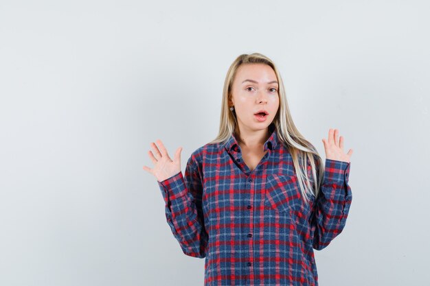 Mulher loira em pose de rendição com camisa e olhando sério, vista frontal.