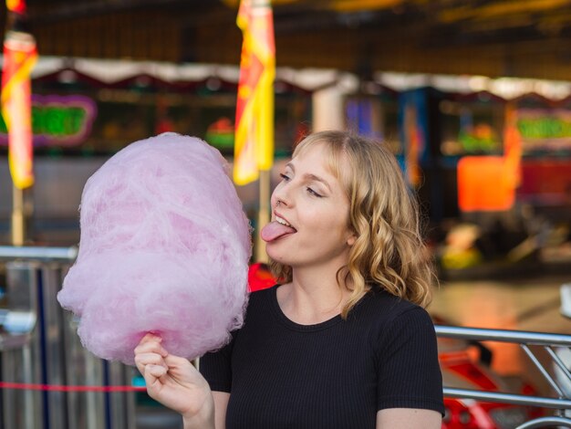 Mulher loira espanhola comendo algodão doce no parque de entretenimento