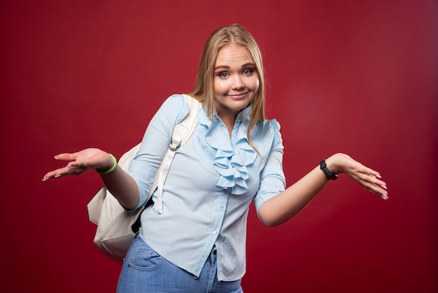 Mulher loira estudante com mochila parece indiferente.