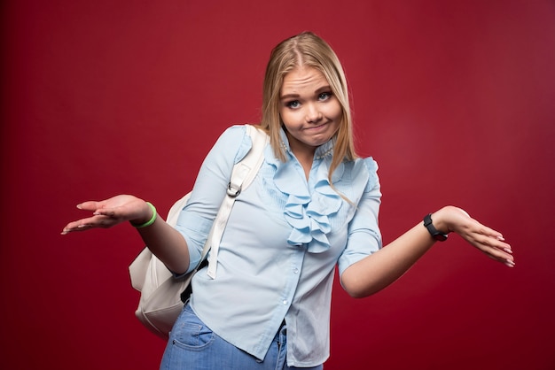 Mulher loira estudante com mochila parece indiferente.