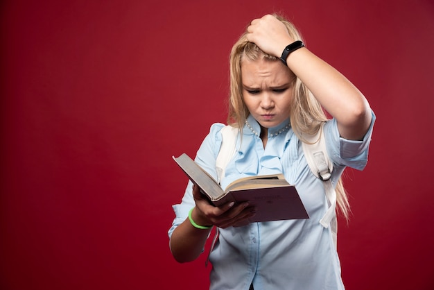 Mulher loira estudante segura seus livros e parece apavorada.