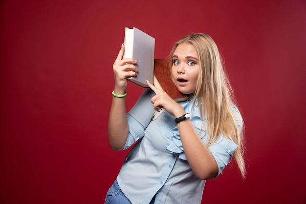 Mulher loira estudante segura seus livros e se sente feliz.