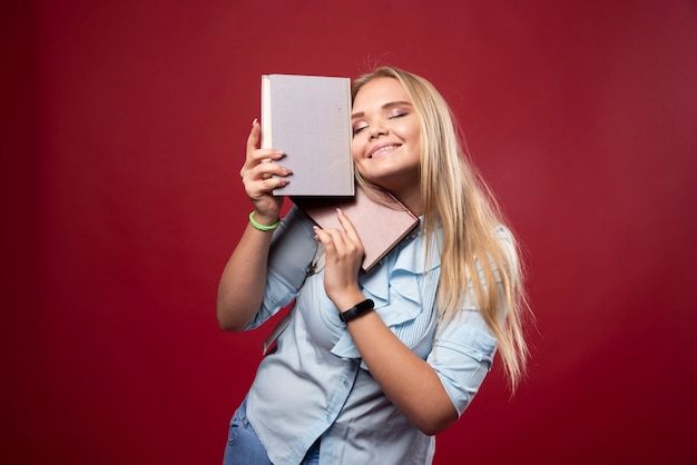 Mulher loira estudante segura seus livros e se sente feliz.