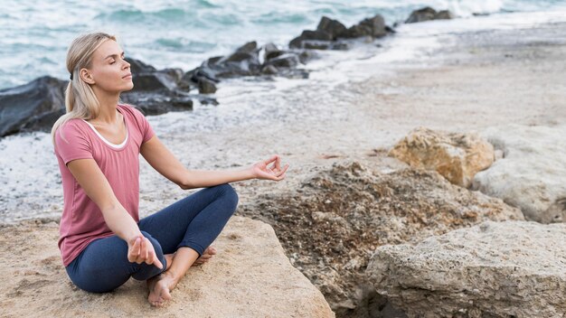Mulher loira fazendo ioga na praia