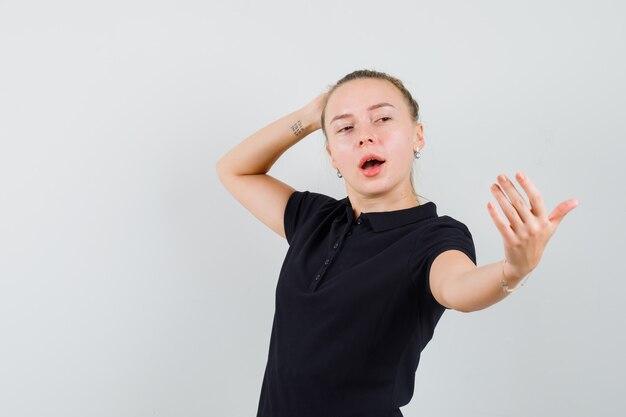 Mulher loira fingindo tirar uma selfie com camiseta preta