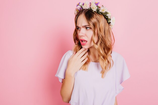 Mulher loira infeliz com guirlanda de flores olhando para longe